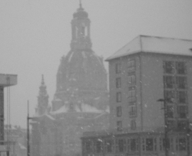 a greyish picture of a building and a church in the back covered in snow