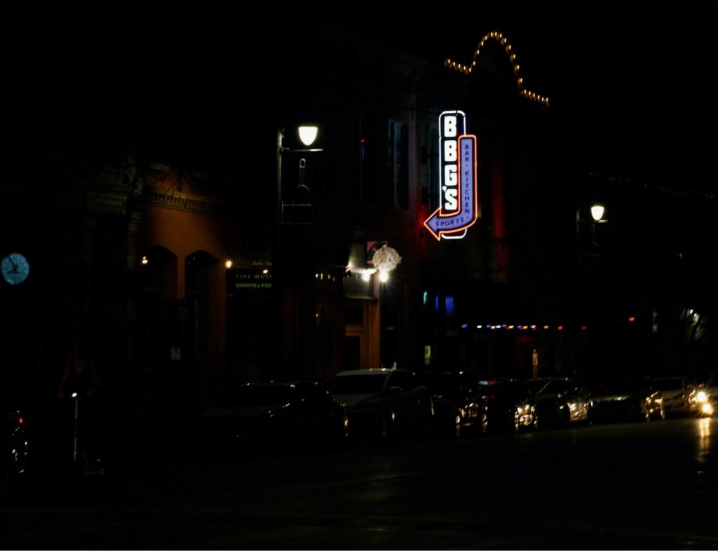 dark image of cars parked on a city street and a sports bar sign